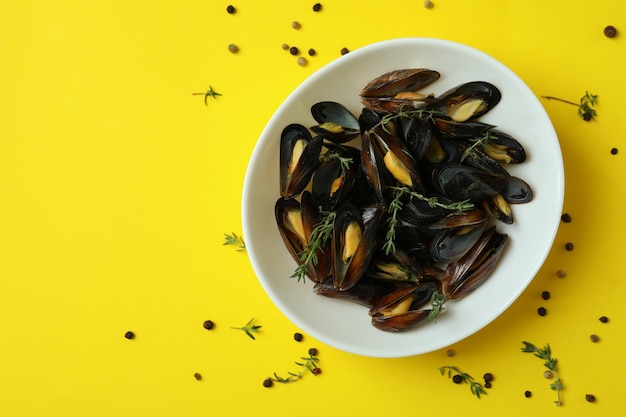 Recipiente con mejillones frescos sobre fondo amarillo