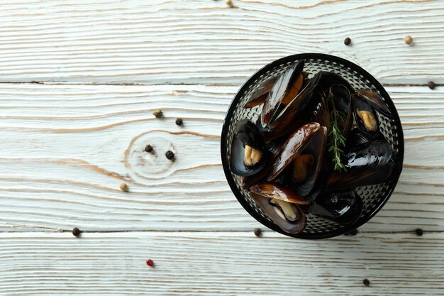 Recipiente con mejillones frescos sobre fondo blanco de madera