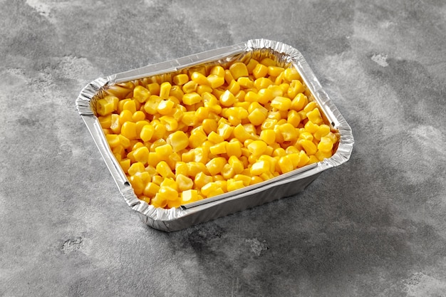 Recipiente de papel de aluminio con granos de maíz hervidos amarillos sobre una mesa de piedra gris