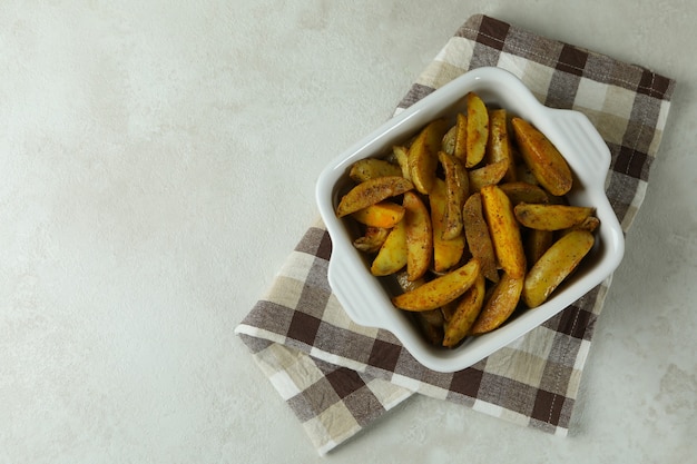 Recipiente con patatas fritas sobre una toalla de cocina, sobre fondo de textura blanca