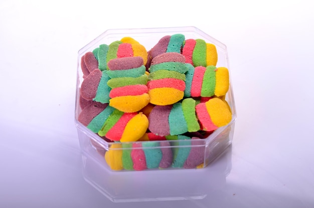 Un recipiente de plástico de caramelos de colores del arco iris se asienta sobre una superficie blanca.