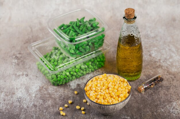 Foto recipiente de plástico con diferentes verduras orgánicas congeladas en la mesa. guisantes, maíz dulce y judías verdes cortadas en una caja