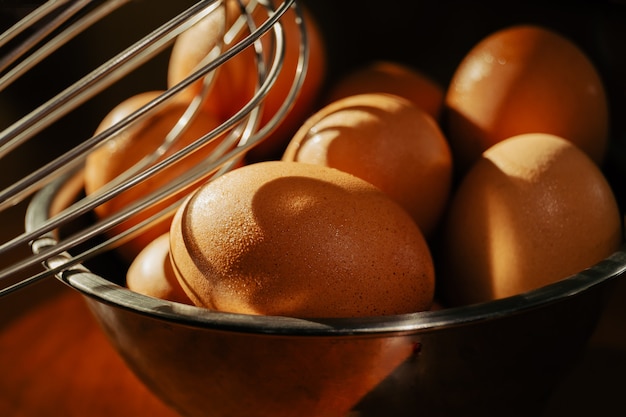 Recipiente de plata con huevos de gallina marrón sobre mesa de madera