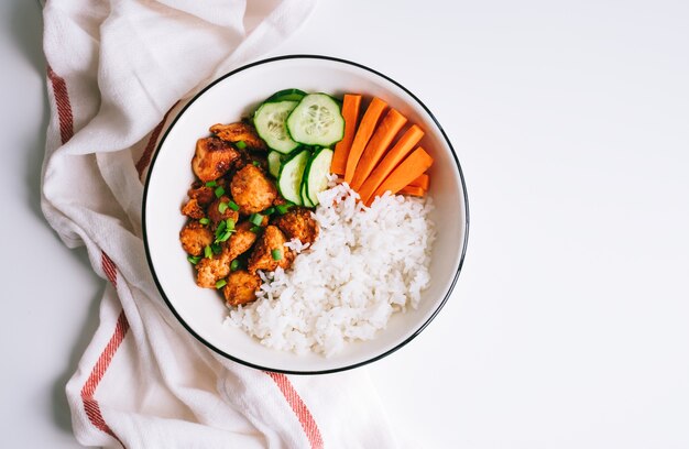 Recipiente saludable con carne de pollo, arroz y verduras en un plato blanco sobre la mesa.