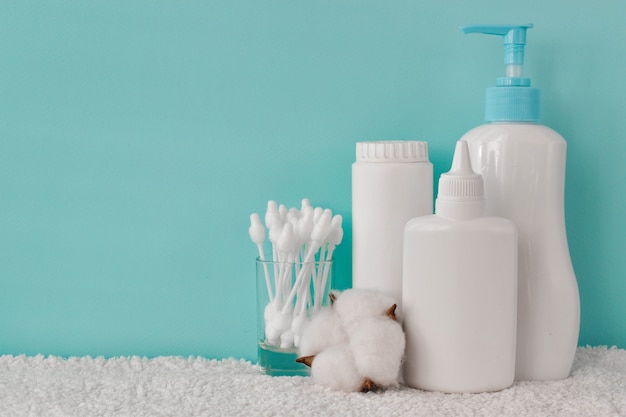 Foto un recipiente con talco para bebés, una botella de talco, jabón líquido y bastoncillos de algodón en un estante.