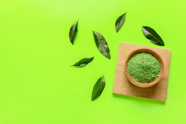 Recipiente con té matcha en polvo y hojas frescas sobre fondo de color
