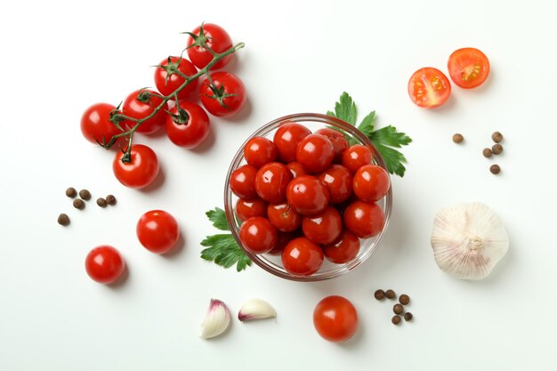 Recipiente con tomates en escabeche e ingredientes sobre fondo blanco.