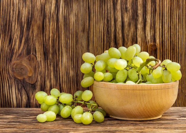 Recipiente con uvas verdes maduras frescas sobre fondo de madera