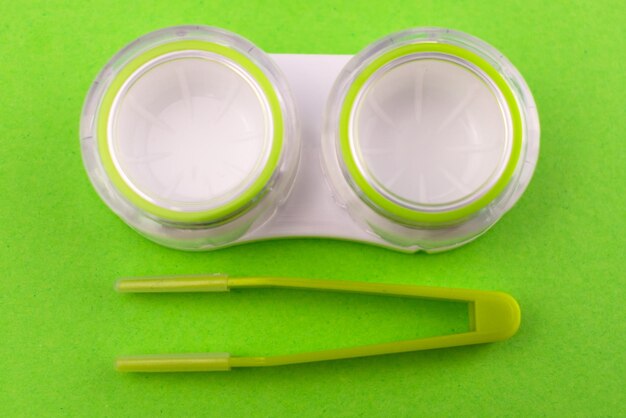 Recipiente verde para lentes de contato e pinças em um fundo verde Closeup