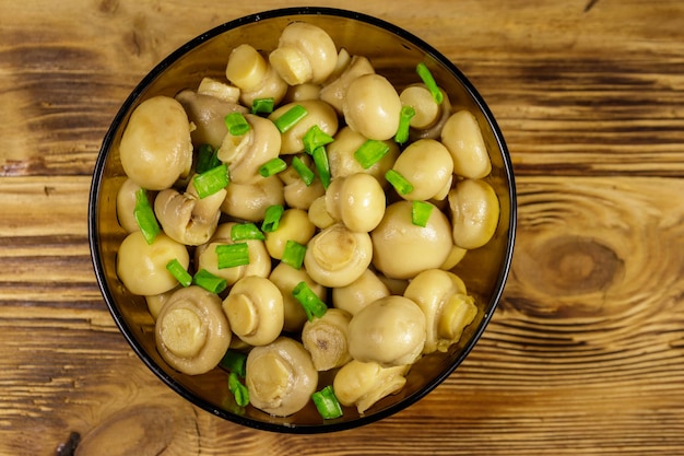 Recipiente de vidrio con champiñones en escabeche. Champiñones marinados en mesa de madera