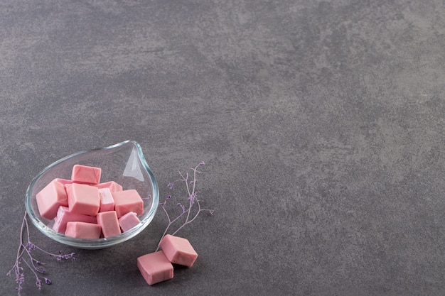 Recipiente de vidrio lleno de malvaviscos en rodajas rosa colocados sobre una mesa de piedra.