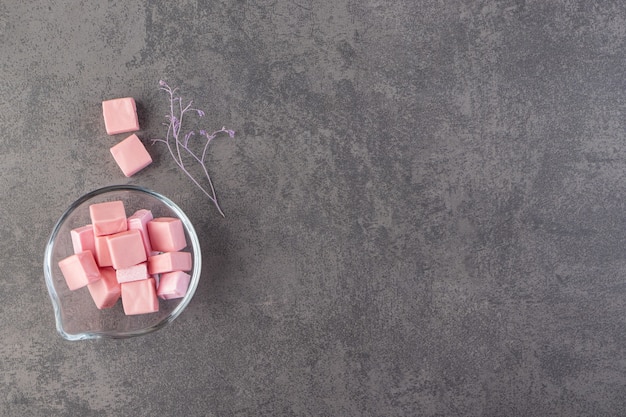 Recipiente de vidrio lleno de malvaviscos en rodajas rosa colocados sobre una mesa de piedra.