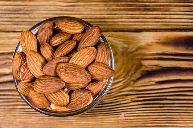 Recipiente de vidrio con nueces de almendras peladas sobre una mesa de madera. Vista superior