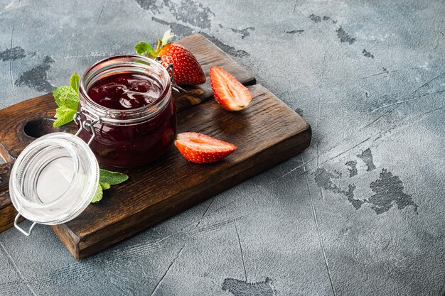 Foto recipiente de vidrio pequeño, de mermelada de frutos rojos, sobre fondo gris con espacio para copiar texto