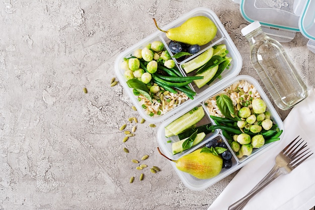 Recipientes veganos de preparación de comidas verdes con arroz, judías verdes, coles de brussel, pepino y frutas.