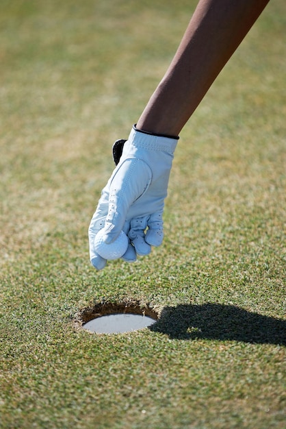 Recoger a mano una pelota de golf del agujero a la luz del sol