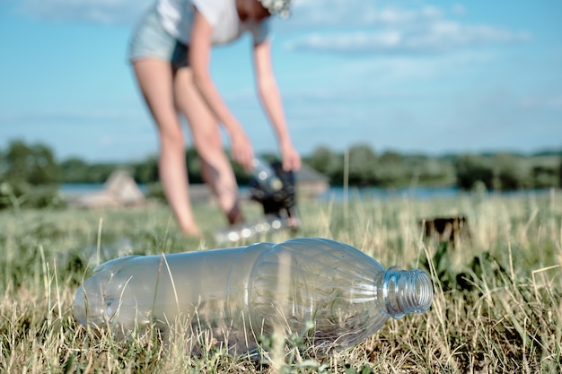 Foto recogiendo basura plástica. la niña recoge botellas de plástico. contaminación ambiental.