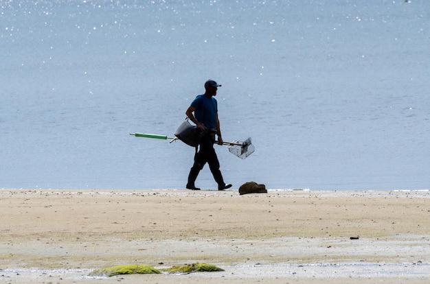 Recolector de mariscos caminando por la orilla de la playa para prepararse para recolectar almejas y mejillones.