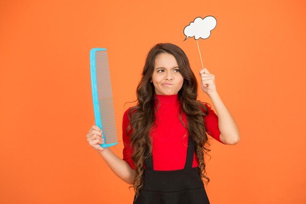 Foto recomendación para el cabello en crecimiento niño con cabello rizado peluquería para niños belleza y moda piense en un nuevo peinado colegiala sostenga un peine grande cuidado y cepille su cabello niña pequeña cabello largo