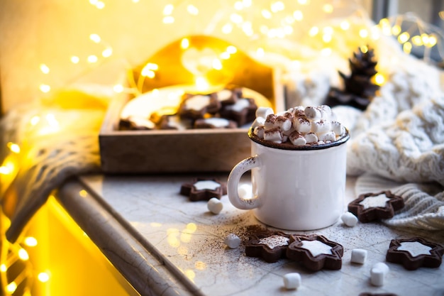 Reconfortante taza de comida navideña de chocolate caliente con malvavisco y galletas con luces acogedoras