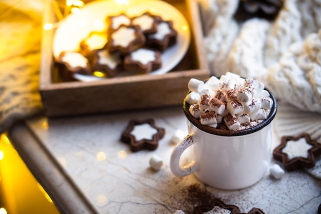 Reconfortante taza de comida navideña de chocolate caliente con malvavisco y galletas con luces acogedoras