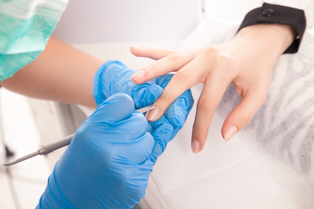 Recorta cerca de manos especialistas haciendo manicura en mano femenina con equipo especial.