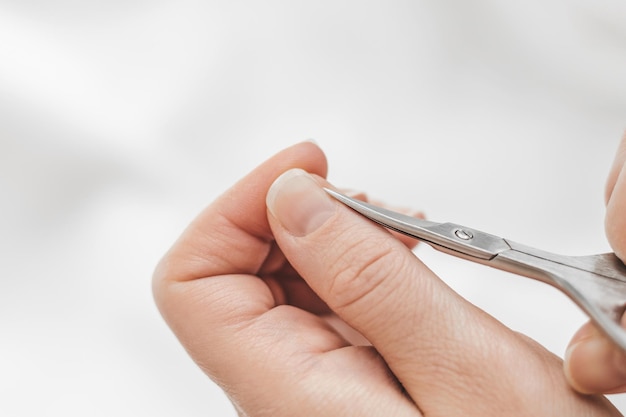 Recorta las cutículas de los dedos Manicura casera La mano de una mujer corta las uñas con tijeras de manicura sobre un fondo blanco Higiene de las uñas Cuidado de las manos