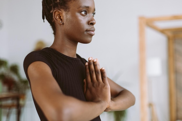 Recortada consciente meditando jovem afro-americana em roupas esportivas pretas praticando mãos de ioga na oração namastê