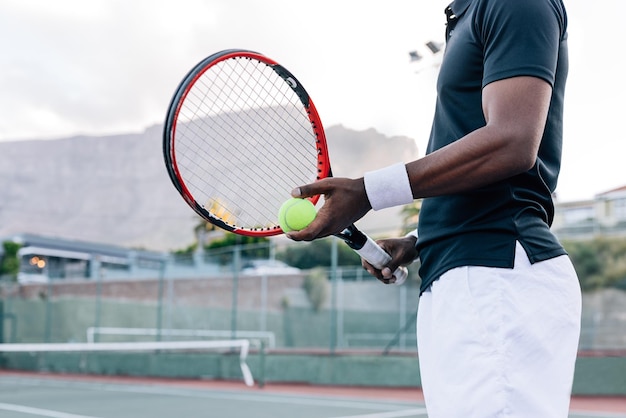 Recortada de un jugador de tenis irreconocible sosteniendo una raqueta y una pelota de tenis mientras está parado al aire libre