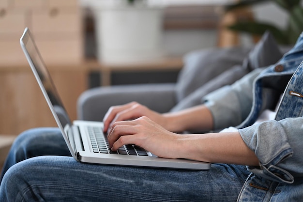 Recortado tiro joven navegando por internet con computadora portátil mientras está sentado en el sofá
