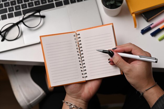 Recortado tiro joven sosteniendo pluma y escribiendo en cuaderno vacío