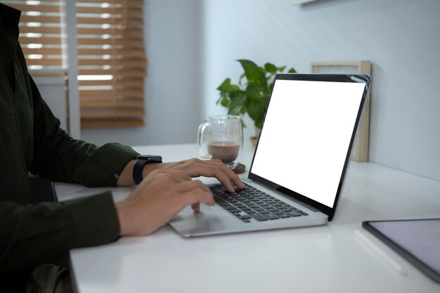 Recortado tiro joven trabajando con computadora portátil en escritorio de oficina blanco