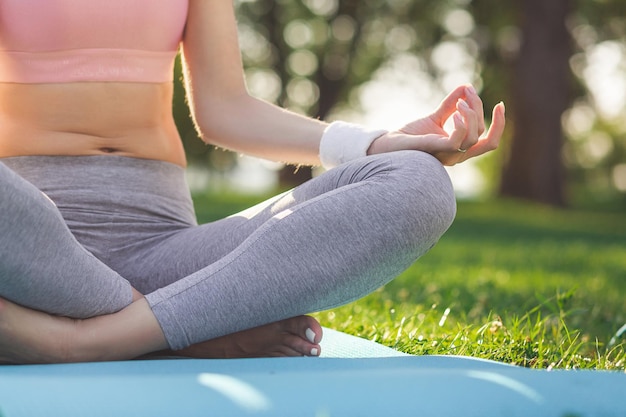 Recortado tiro de mujer sentada en posición de loto en la estera de yoga en el parque