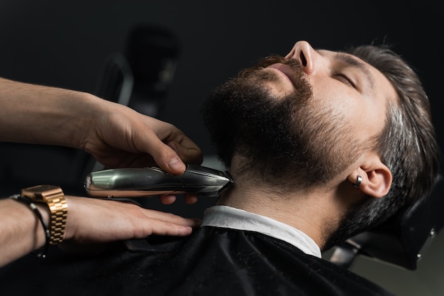 Recortar la barba con una máquina de afeitar. Publicidad para peluquería y salón de belleza masculina.