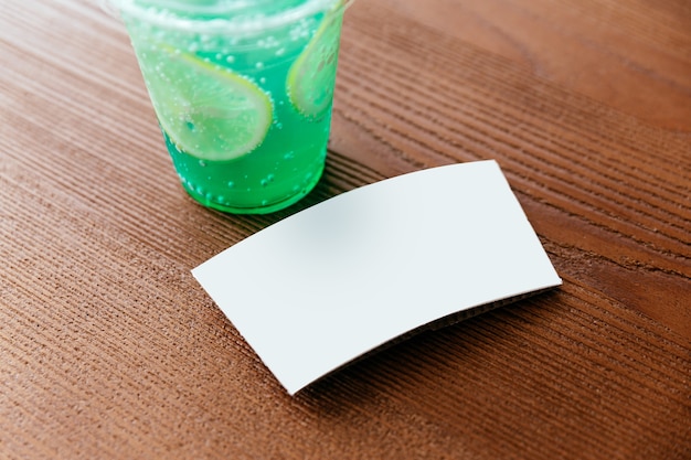 Recortar imagen de la manga de la taza blanca de refresco helado verde con rodajas de limón sobre una mesa de madera.