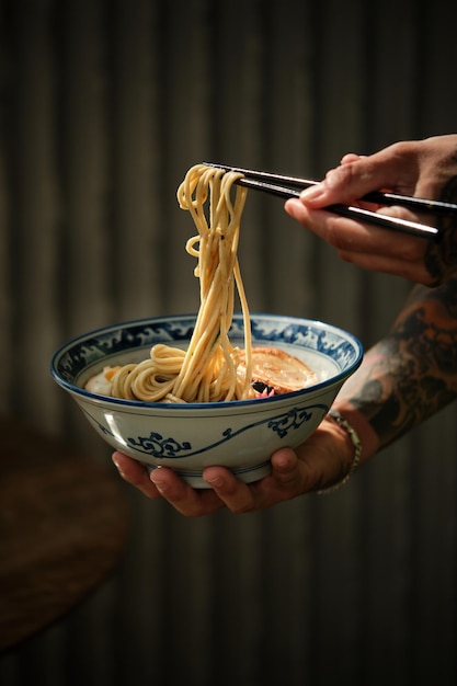 Recortar persona anónima con palillos comiendo deliciosa sopa de ramen con caldo caliente del tazón en el restaurante