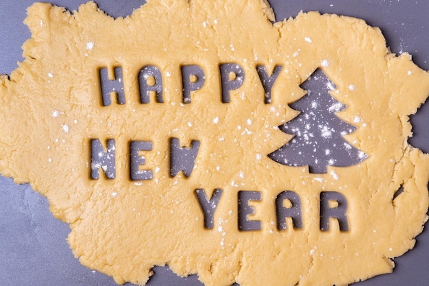 Recorte de massa de biscoito em forma de letras do texto Feliz Ano Novo e árvore de Natal polvilhada com farinha