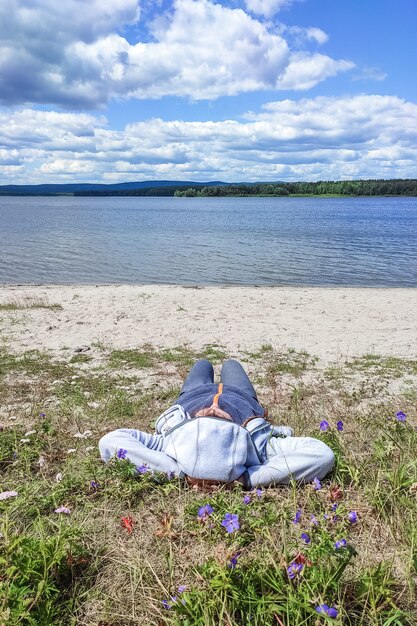 Foto recreación al aire libre la niña está acostada en la hierba con flores en la orilla de un lago del bosque