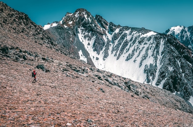 Recreación extrema y turismo de montaña. Un excursionista masculino por el sendero de la montaña. Al fondo, grandes montañas nevadas. Copie el espacio.