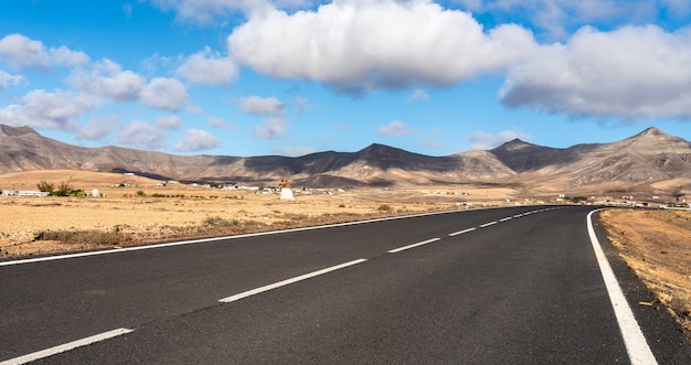 Recto del camino infinito, con el mar en el horizonte con montañas en un paisaje árido