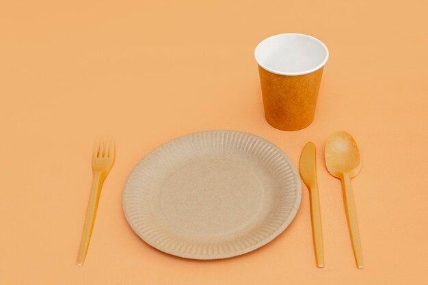 Recycelbare Gabel, Löffel, Messer, Teller und Tasse auf beigem Hintergrund. Küchenutensilien. Ansicht von oben. Minimalistischer Stil. Platz kopieren