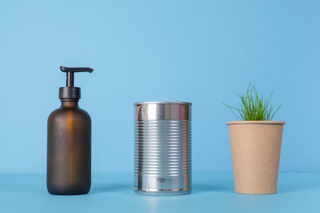 Recycling von Pappbechern, Zinnprodukten, gebrauchten Glasprodukten auf blauem Hintergrund, aus denen Sprossen sprossen