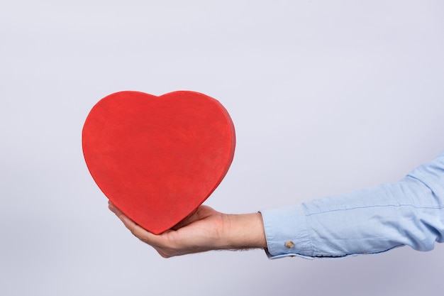 Red Box Herzform in der Hand, weißer Hintergrund. Geschenk für Geliebte. Geschenk zum Valentinstag