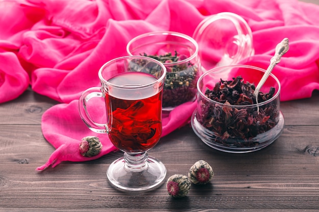 Red Hot Hibiscus Tee in einem Glasbecher auf einem Holztisch und trockenem Tee Vanillepudding