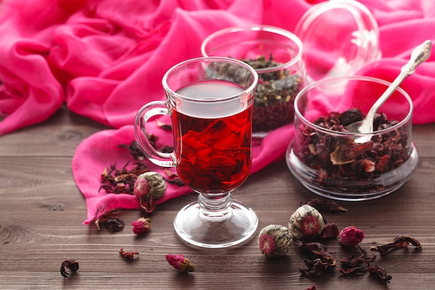 Red Hot Hibiscus Tee in einem Glasbecher auf einem Holztisch und trockenem Tee Vanillepudding