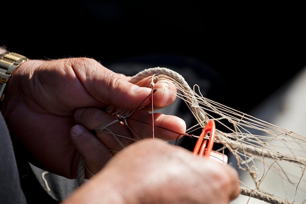 red de pesca en manos del pescador, teje y repara cosiendo las redes con una aguja y th