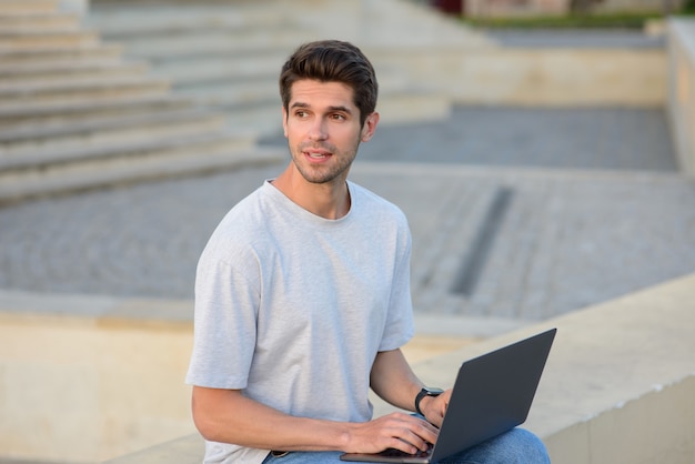 Redactor independiente joven que usa la computadora portátil que trabaja en línea que se sienta al aire libre