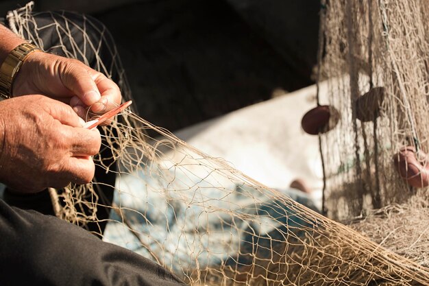 rede de pesca nas mãos do pescador, ele tece e repara costurando as redes com uma agulha e