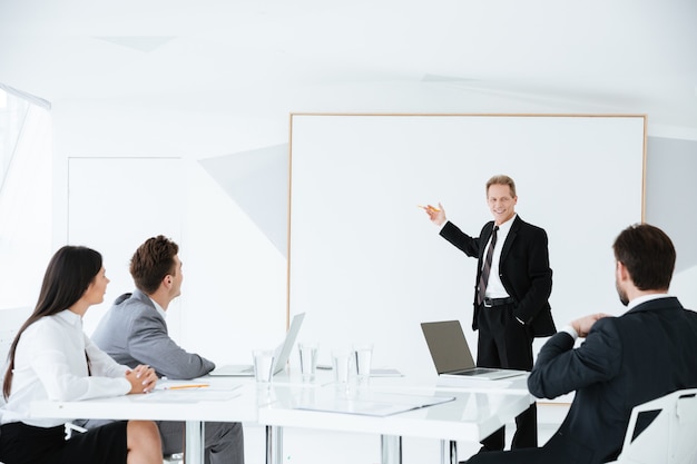 Rede eines älteren Geschäftsmannes auf einer Konferenz, die mit seinen Kollegen am Tisch in der Nähe des Vorstands steht