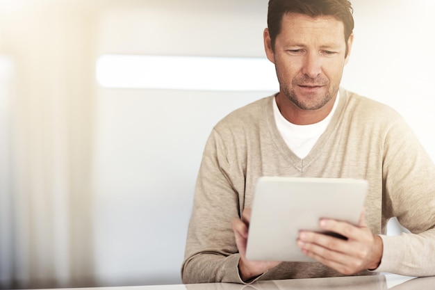 Rede social madura e homem com tablet e à mesa em sua casa Blog ou tecnologia de conectividade com a Internet e espaço de maquete com pessoa do sexo masculino lendo um e-mail ou relatório na mesa de sua casa